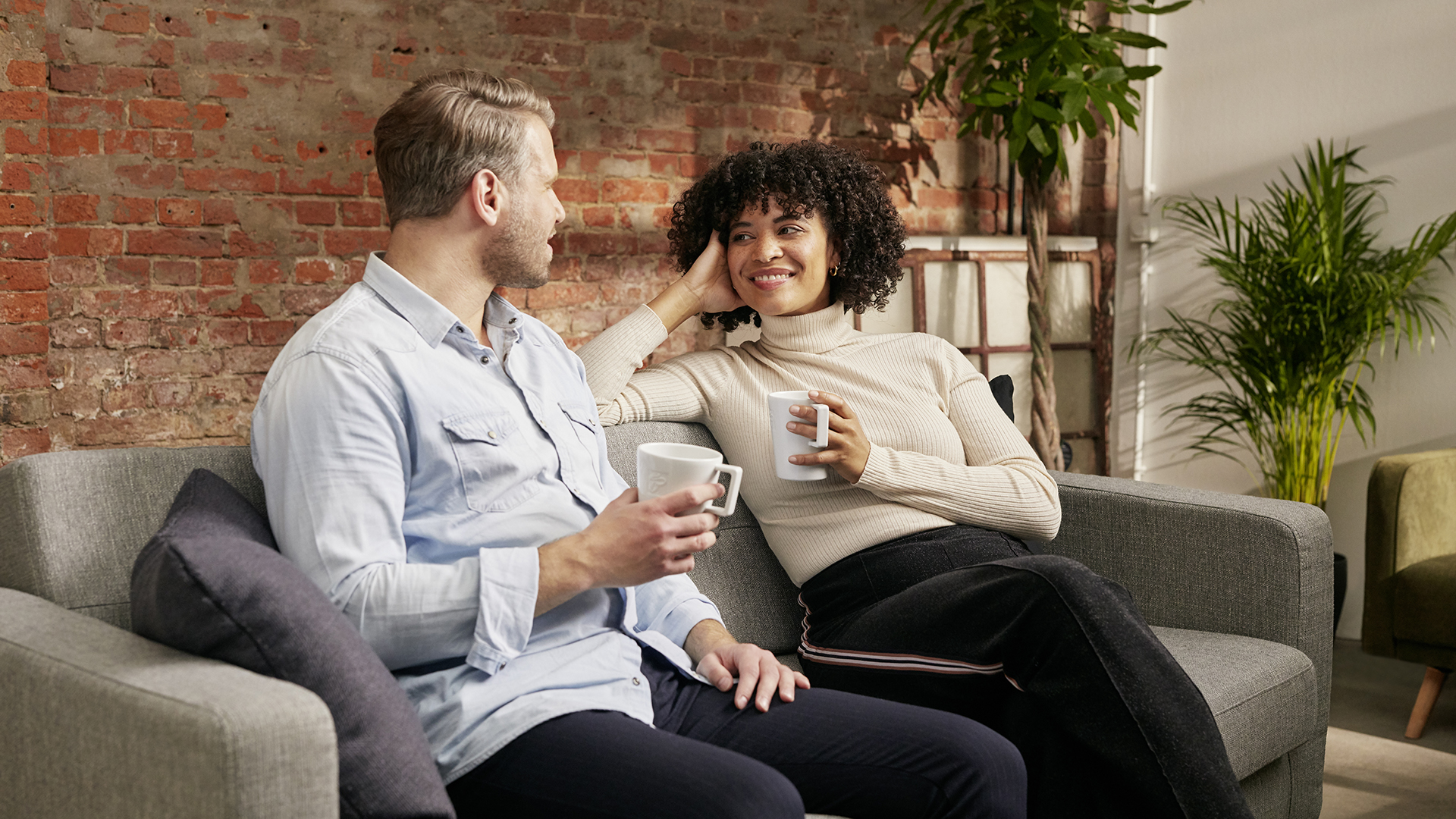 Frau und Mann sitzen auf einem Sofa zusammen und trinken Kaffee. Bei lächeln.